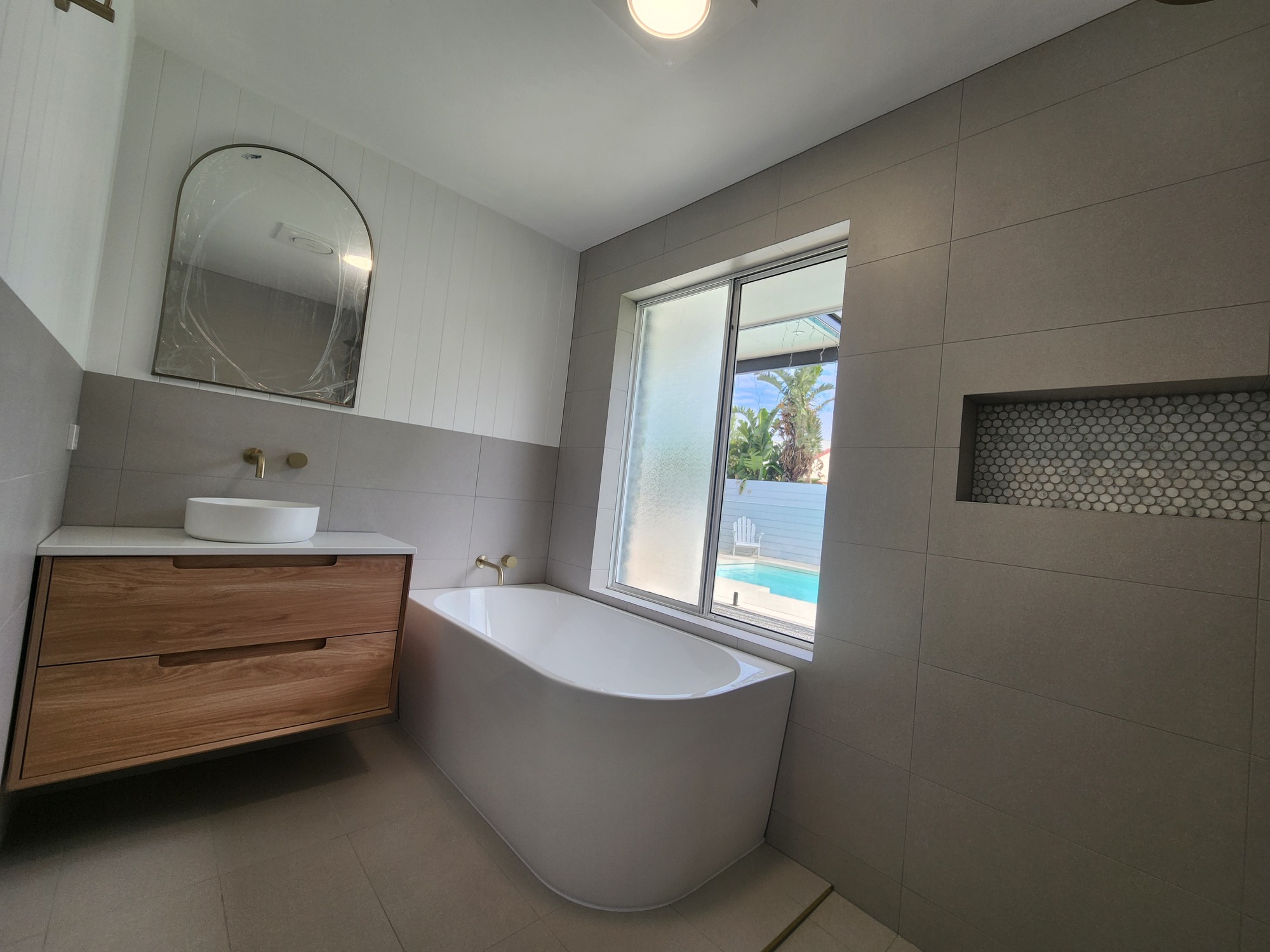 Completed bathroom with freestanding bath, floating timber vanity and large-format grey tiling