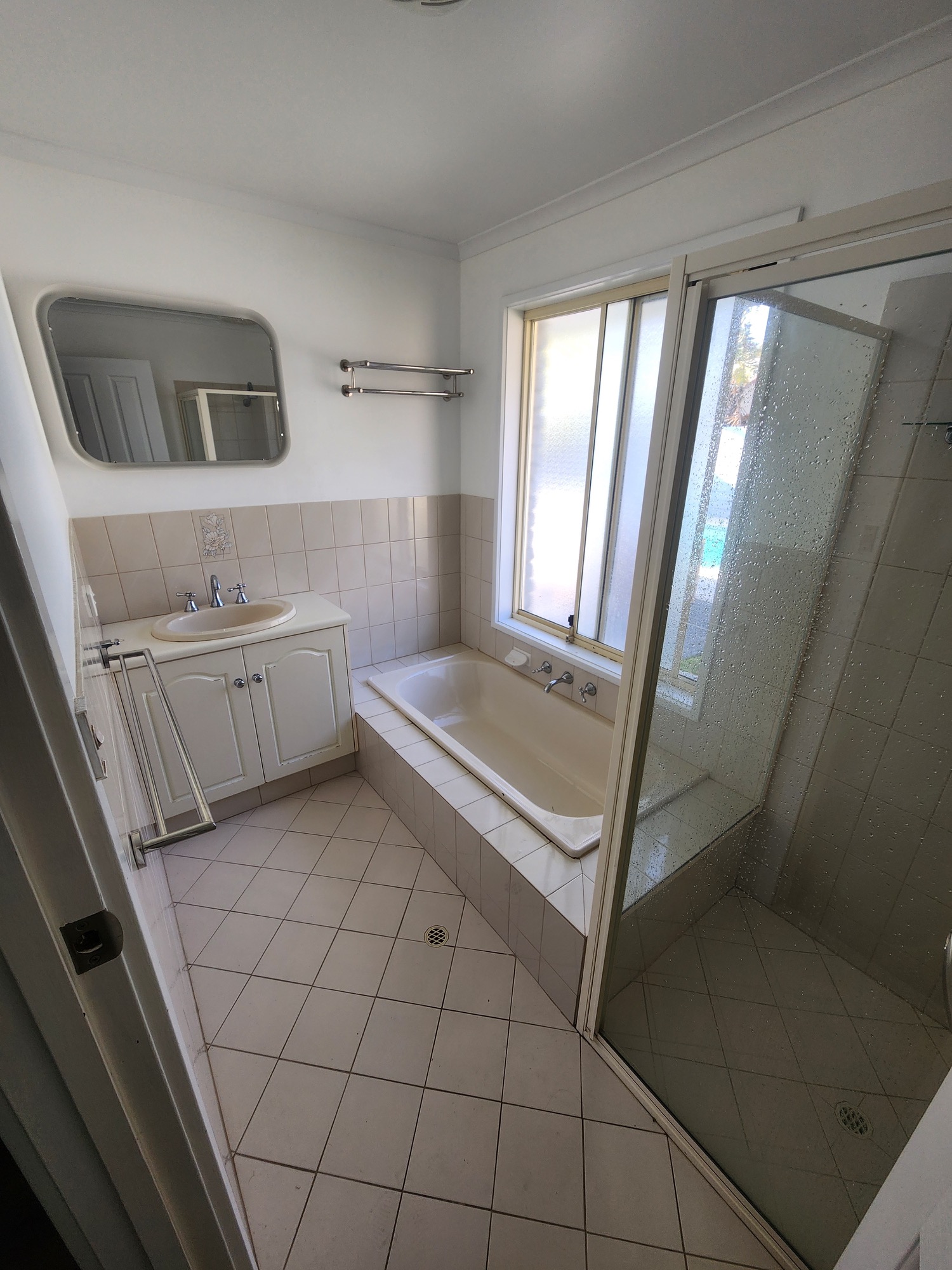 Original bathroom with boxed-in bath, framed shower, floor-standing vanity and small-format tiles
