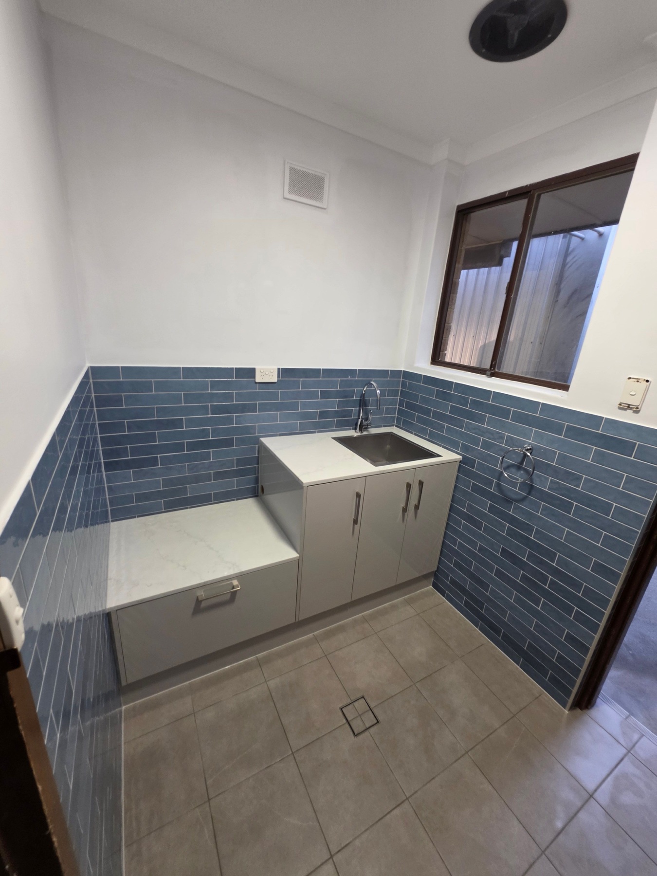 Finished laundry with blue tiled walls, grey cabinetry and inset sink