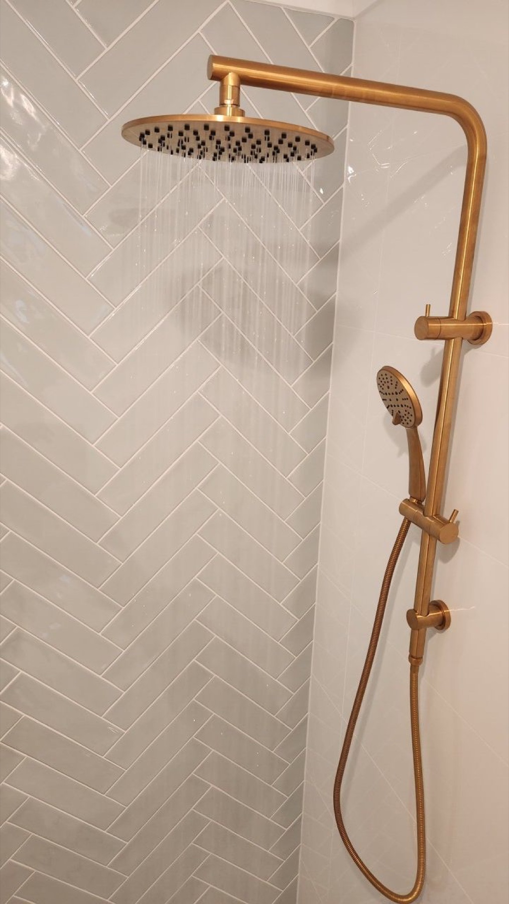 Brushed-brass shower fitting against pale herringbone tiles