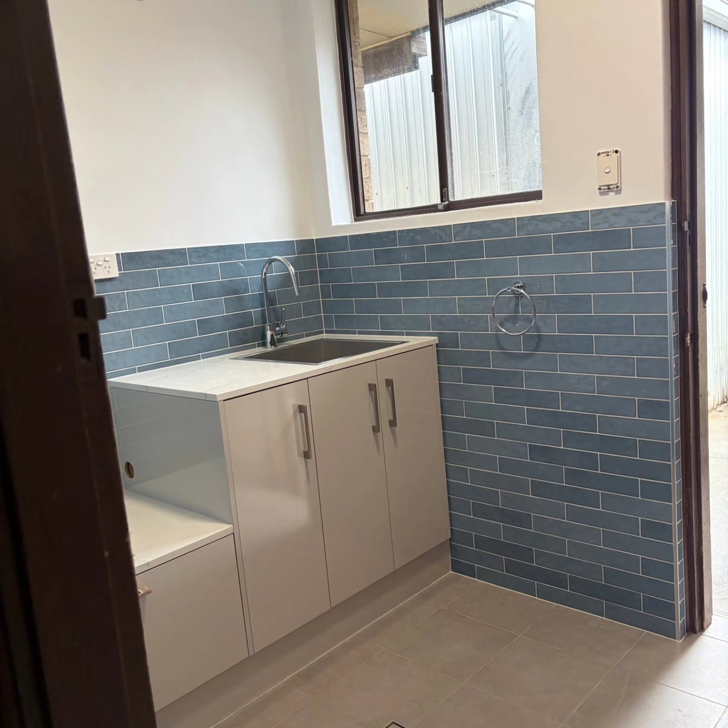 Completed laundry with blue tiles and white cabinetry
