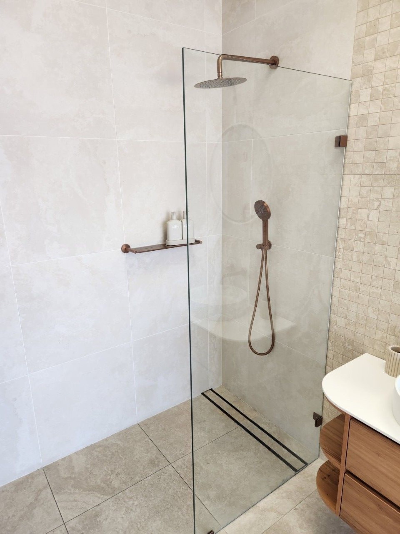 Completed frameless shower with large-format tiles and brushed-brass fittings