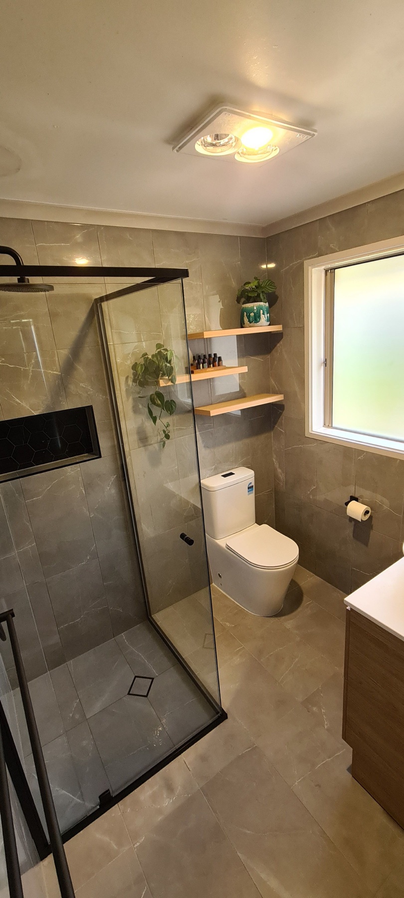 Grey-tiled bathroom with black-framed shower, toilet and timber shelving