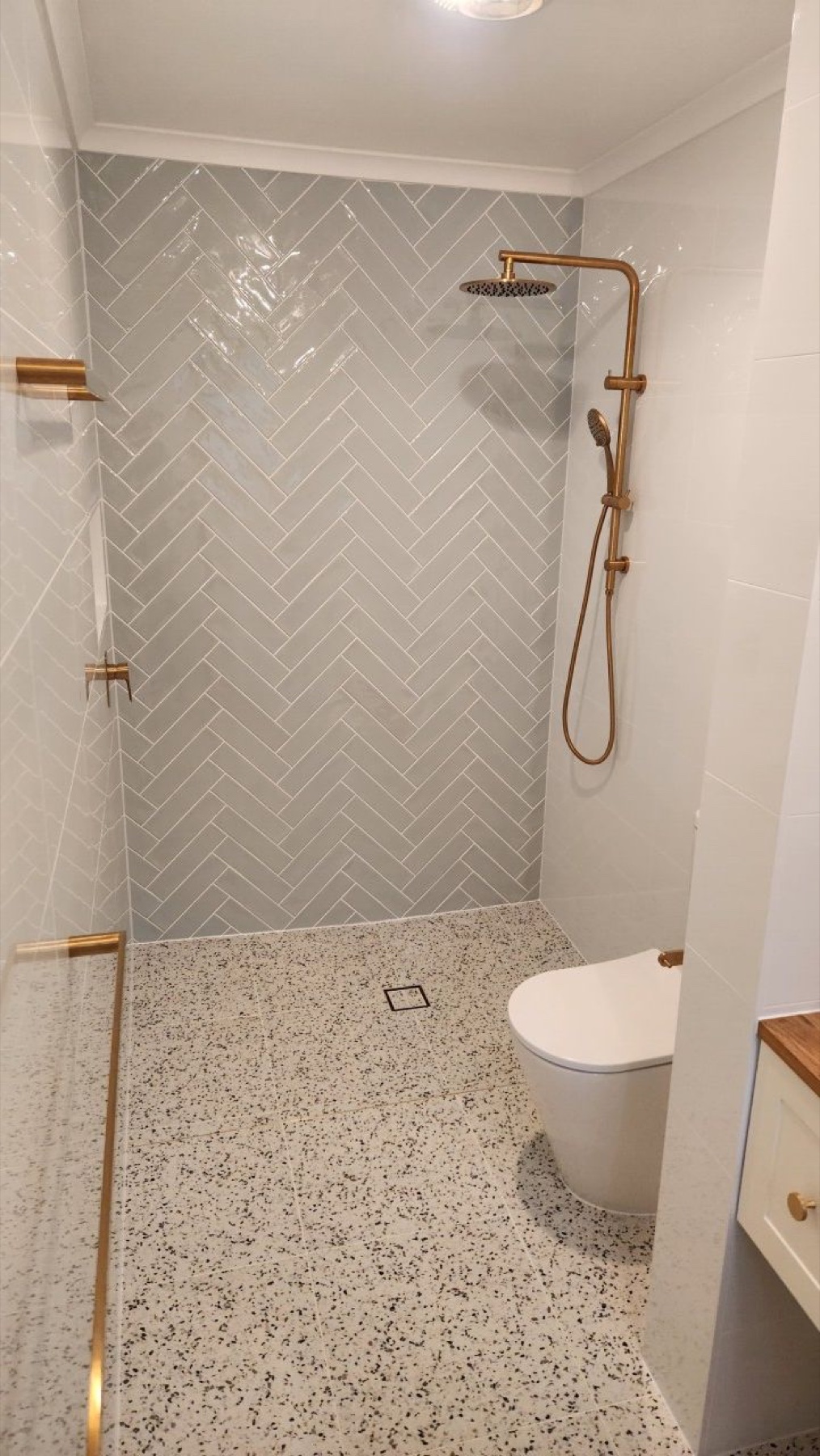 Walk-in shower with grey herringbone tiles, terrazzo floor and brushed-brass fittings