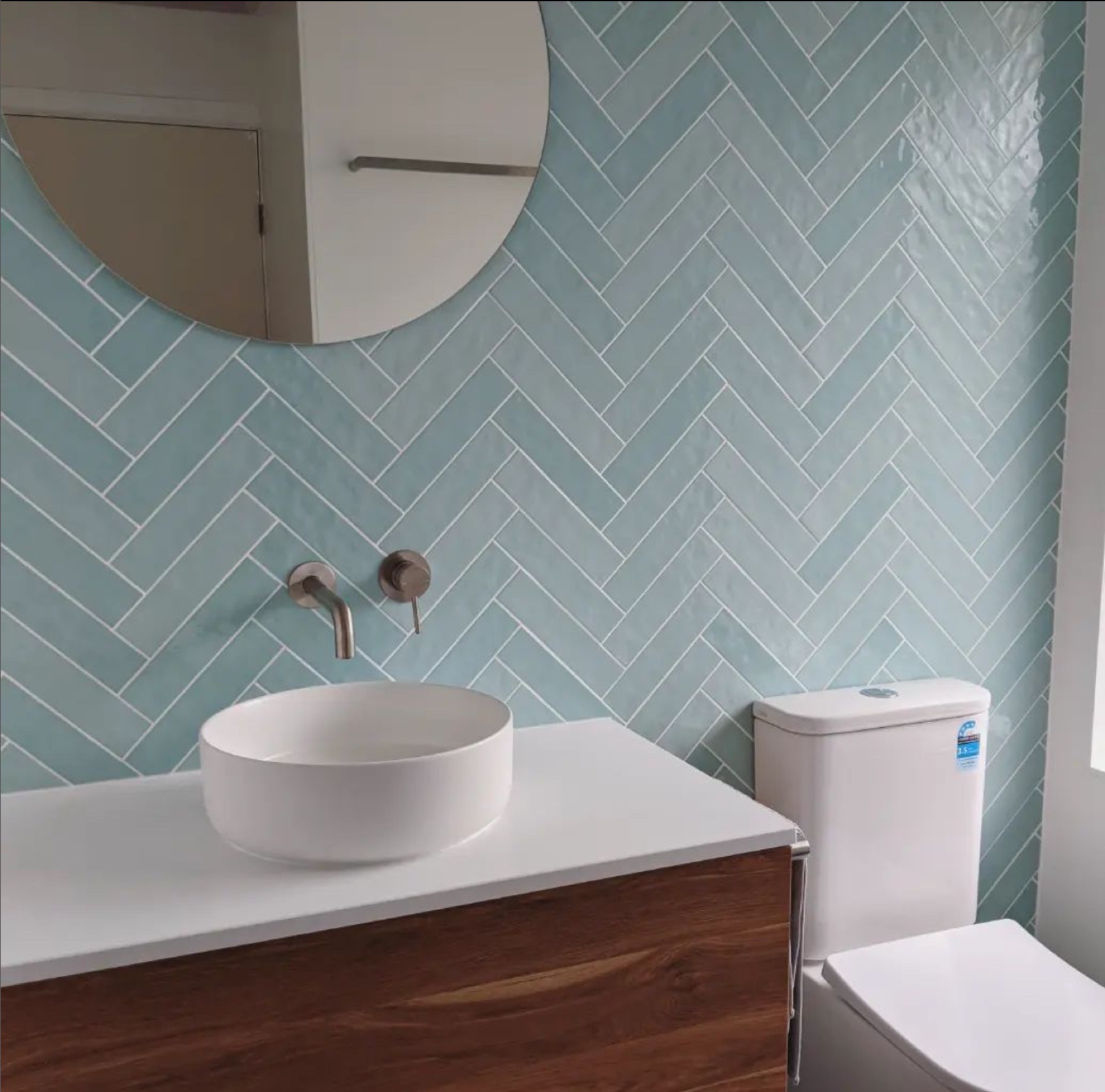 Ensuite vanity with timber cabinetry and a seafoam herringbone tiled wall