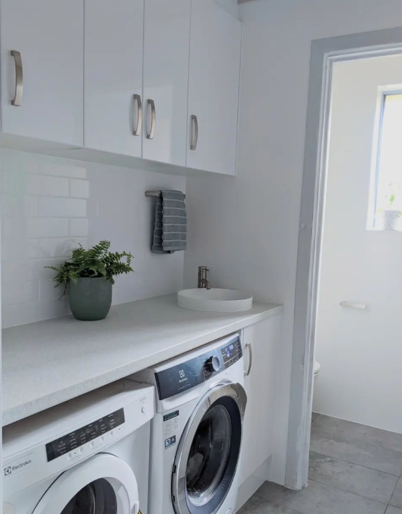 Finished white laundry with overhead cabinetry, appliances and a tiled splashback