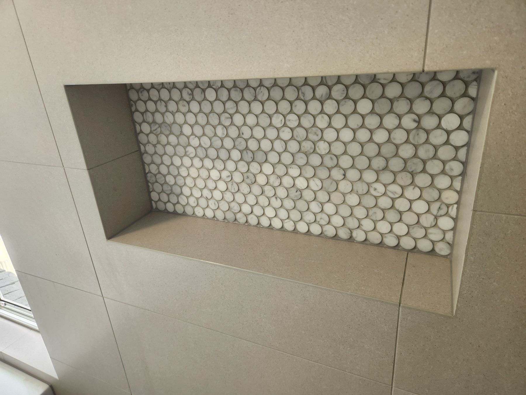 Recessed shower niche finished with round pebble mosaic tiles